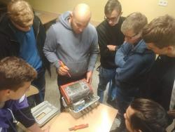 Na zdjęciu grupa uczniów , pod okiem instruktora, przygotowuje się do montażu instalacji fotowoltaicznej.
