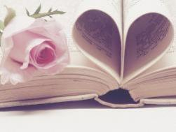 Na otwartej książce leży różowa róża, a z kilku stron jest zrobione serce