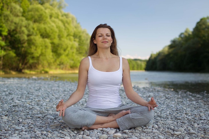 joginka medytuje, siedzi na kamieniach, za nią woda