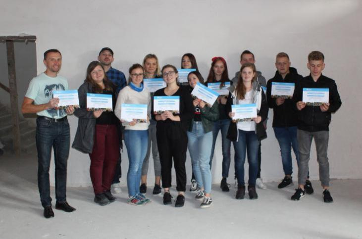 Na tlebiałej ściany uczniowie oraz pracownicy Habitat for Humanity po zakończonej pracy. W rękach trzymają dyplomy z podziękowaniami za pracę.