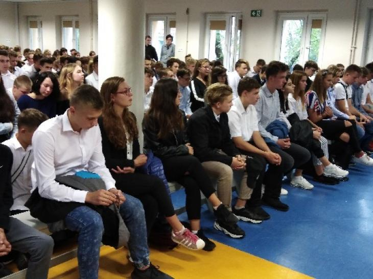 Zdjęcie przedstawia grupę młodzieży klas pierwszych w strojach galowych, zgromadzonych w auli szkolnej podczas uroczystości ślubowania klas pierwszych
