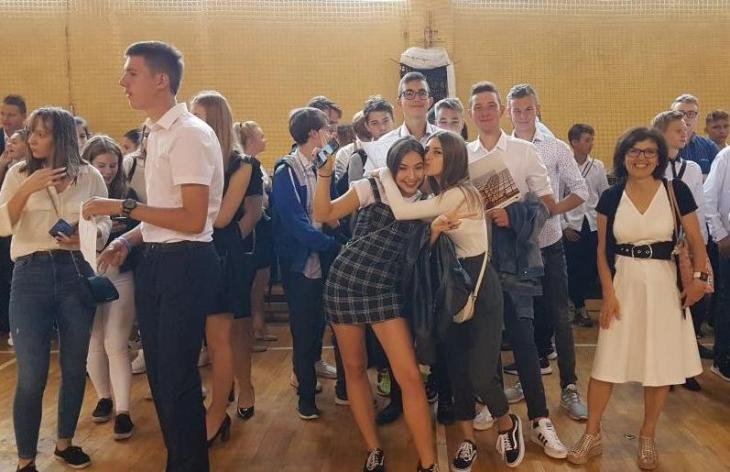 Grupa roześmianych uczniów oczekuje w sali gimnastycznej na uroczystość rozpoczęcia roku szkolnego 2019/2020