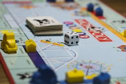 Plansza do gry w Monopoly, na której stoją pionki - autka, kostka do gry oraz leżą karty