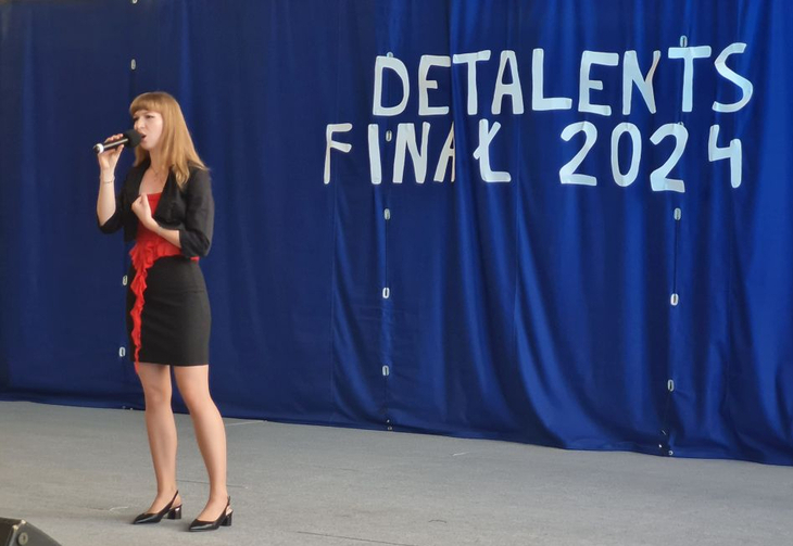 Karolina podczas występu, za nią na granatowym tle napis DeTalents 2024