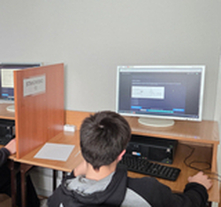 Zdjęcie przedstawia uczestników Olimpiady Wiedzy Elektrycznej „ElektroChallenge”, którzy w skupieniu rozwiązują zadania przy komputerowych stanowiskach konkursowych