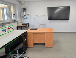 Na zdjęciu widać pracownię OZE z biurkiem, stanowiskiem laboratoryjnym, monitorem na ścianie oraz szafą na sprzęt. Pomieszczenie jest jasne i przygotowane do zajęć praktycznych.