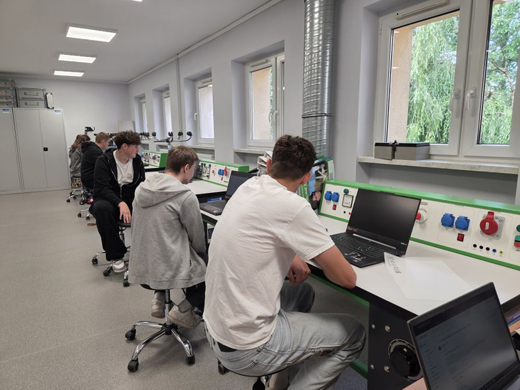 Na zdjęciu uczniowie uczestniczą w zajęciach praktycznych w nowoczesnej pracowni technicznej. Pracując przy stanowiskach wyposażonych w sprzęt i instalacje dydaktyczne, rozwijają umiejętności zawodowe oraz zdobywają praktyczne doświadczenie potrzebne w przyszłej pracy.