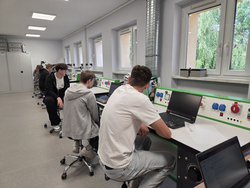 Na zdjęciu uczniowie uczestniczą w zajęciach praktycznych w nowoczesnej pracowni technicznej. Pracując przy stanowiskach wyposażonych w sprzęt i instalacje dydaktyczne, rozwijają umiejętności zawodowe oraz zdobywają praktyczne doświadczenie potrzebne w przyszłej pracy.