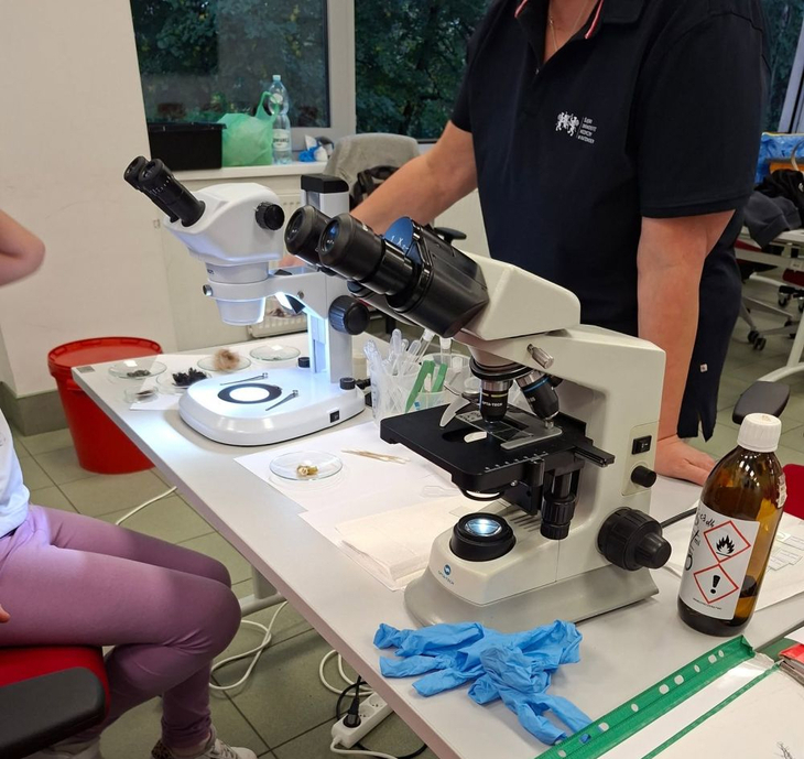 Na zdjęciu widać stanowisko laboratoryjne z mikroskopami, preparatami oraz wyposażeniem do pracy badawczej. Uczestnicy wydarzenia mogli przyjrzeć się z bliska pracy laboratoryjnej i poznać podstawy badań mikroskopowych.